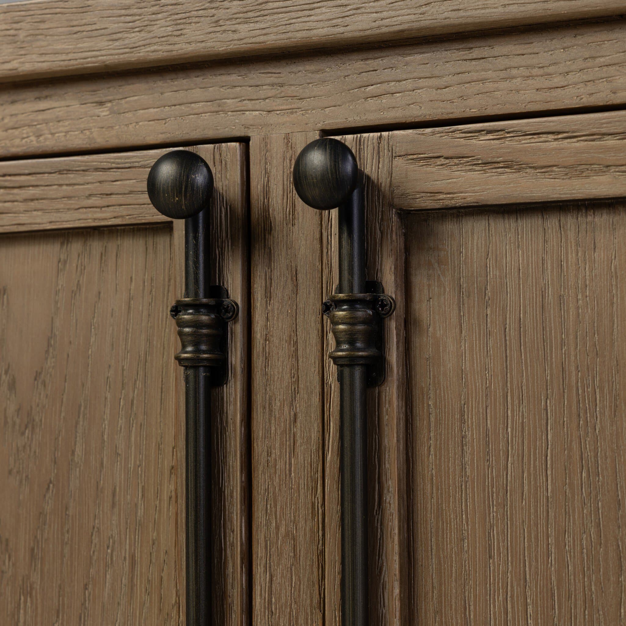 A close-up view of two cabinet doors, constructed from light brown, visibly distressed wood. Each door is fitted with a vertically oriented, dark bronze-finished pull handle featuring a spherical top and an ornate, ribbed cylindrical base. — 3D model