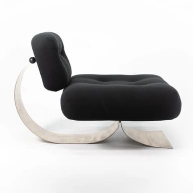 A postmodern lounge chair featuring a distinctive sculptural brushed metal base supporting a plush, black upholstered seat and backrest. The base is formed by a continuous, wide C-shaped metal band that curves elegantly from the floor, up to support the back, and then back down to form the front leg structure. The seat and back are generously padded and upholstered in black fabric, with subtle button tufting on the seat. The backrest is affixed to the metal support with visible hardware, including two black spherical elements. — 3D model