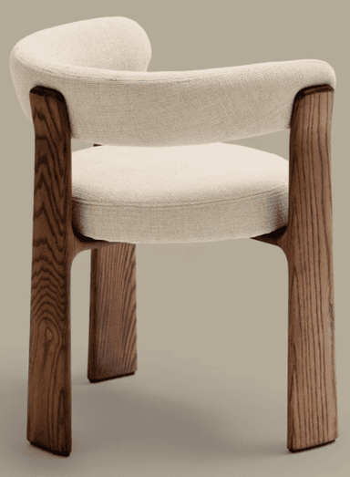 A modern armchair with a curved upholstered backrest and seat, supported by four solid wood legs. The legs have a distinct organic shape and visible wood grain. The upholstery is a textured, light-colored fabric. The design is minimalist and contemporary. — 3D model