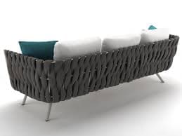 A modern three-seater sofa featuring a clean, minimalist design. It has a generously cushioned base and three loose back cushions upholstered in a light grey or white fabric. The distinctive armrests and a partial backrest are crafted from dark grey woven rope or synthetic cord, providing a textural contrast. The sofa is supported by slender, splayed metal legs with a light finish. — 3D model