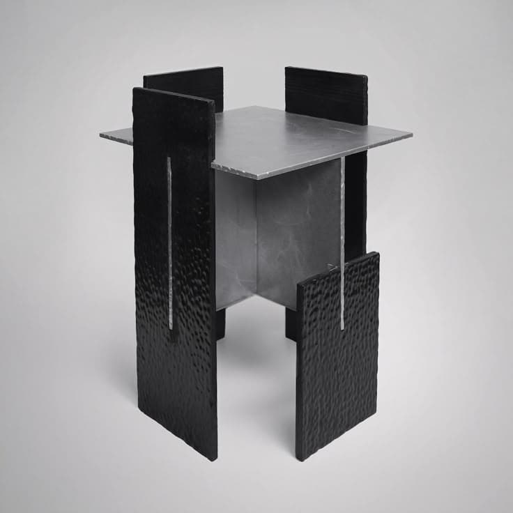An angular end table with a square metallic top supported by a central column. The base consists of four vertical, textured black panels that extend upwards and outwards, creating a distinctive, sculptural form. Each black panel has a vertical groove near its center. — 3D model