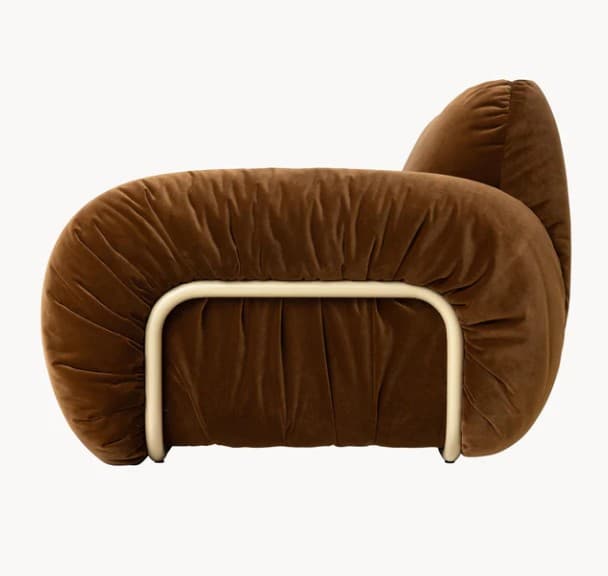 A plush, sculptural armchair upholstered in a rich brown velvet fabric. The armchair features an organic, rounded silhouette with ample cushioning that appears to be gathered or shirred, creating a textured effect. A tubular metal frame, finished in a light, possibly cream or off-white color, is visible beneath the upholstery, providing structural support and a contrasting element. The design evokes a contemporary, possibly retro-inspired aesthetic. — 3D model
