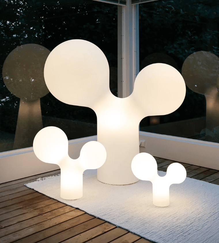 A modern white table lamp featuring an abstract, organic form that resembles a stylized plant or cloud. It consists of a cylindrical base from which two rounded, bulbous forms emerge, with the larger one extending upwards and a smaller one branching off to the side. The entire structure is illuminated from within, providing a soft, diffused glow. — 3D model