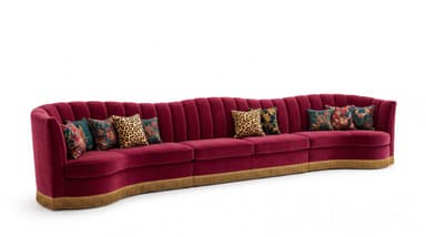 A luxurious and expansive curved sectional sofa upholstered in deep red velvet, featuring a distinctive channel-tufted backrest and a decorative gold-toned fringe trim along its base. The sofa is composed of multiple curved segments that form a continuous, sweeping line. It is adorned with several throw pillows in contrasting patterns, including leopard print and floral designs, adding to its opulent aesthetic. — 3D model