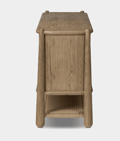 A rustic light oak sideboard featuring four cabinet doors with exposed wood grain and small black knob handles. The main cabinet rests on an elevated frame that extends to form the legs, with a woven cane shelf integrated into the lower structure. The wood has a natural, slightly weathered finish and rounded edges. — 3D model