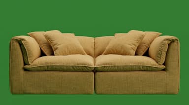 A contemporary light gray two-seater sofa, composed of two modular sections, featuring a low profile and plush, inviting design. It has wide arms and backrests, complemented by multiple loose back cushions and accent pillows, all upholstered in a textured fabric with visible piping along the seams. — 3D model