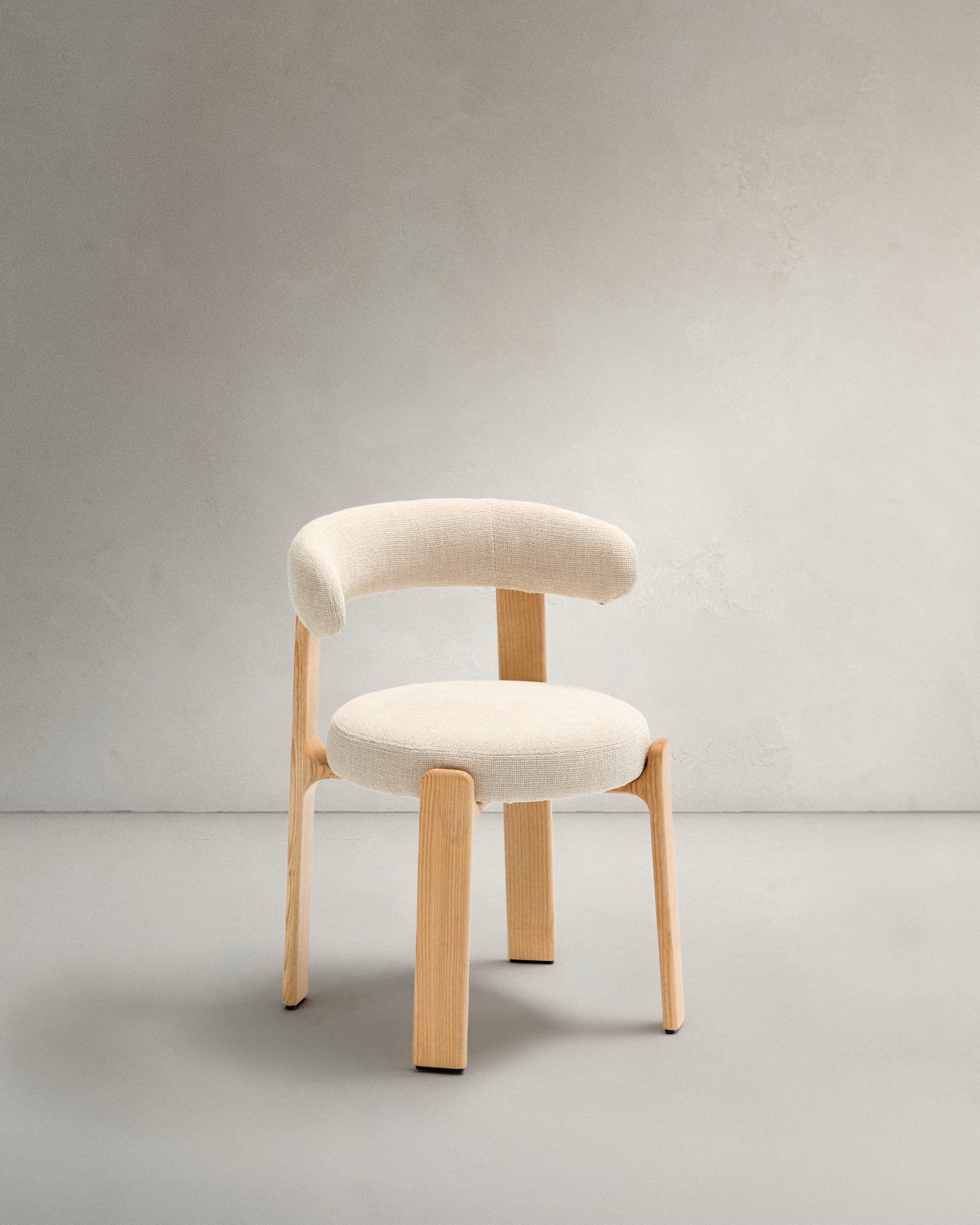 A contemporary armchair featuring a light wood frame and cream-colored upholstered seat and backrest. The design is minimalist with rounded forms, including a circular seat and a curved backrest that seamlessly integrates with the armrests. The legs are sturdy, splayed outwards slightly, and match the natural wood tone. — 3D model