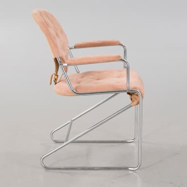 A cantilever armchair with a tubular chrome-plated steel frame. The seat, backrest, and armrests are upholstered in a tufted, salmon-pink, velvety fabric. The backrest has a distinct curved shape and is attached to the frame with leather straps. The armrests are also padded and follow the curvature of the frame. — 3D model