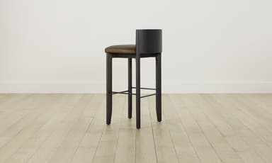 A modern bar stool featuring a dark stained wooden frame and a padded, upholstered seat with a low backrest. The stool has four sturdy, slightly tapered legs and an integrated metal footrest. — 3D model