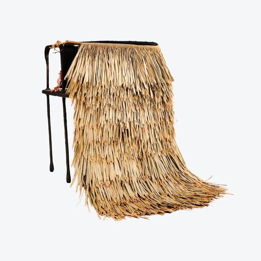 A side table with a dark, metallic frame featuring two thin legs on the visible side. The tabletop is obscured by a long, draped skirt made of dried grass or palm fronds. The grass material is layered and reaches the floor, creating a voluminous effect. There are visible red beads and rope details on the frame near the top. — 3D model