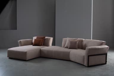 A contemporary modular sectional sofa upholstered in a light beige textured fabric, featuring a left-hand chaise lounge and a right-hand armrest with a distinctive dark framed detail. It is adorned with several brown and beige throw pillows. — 3D model