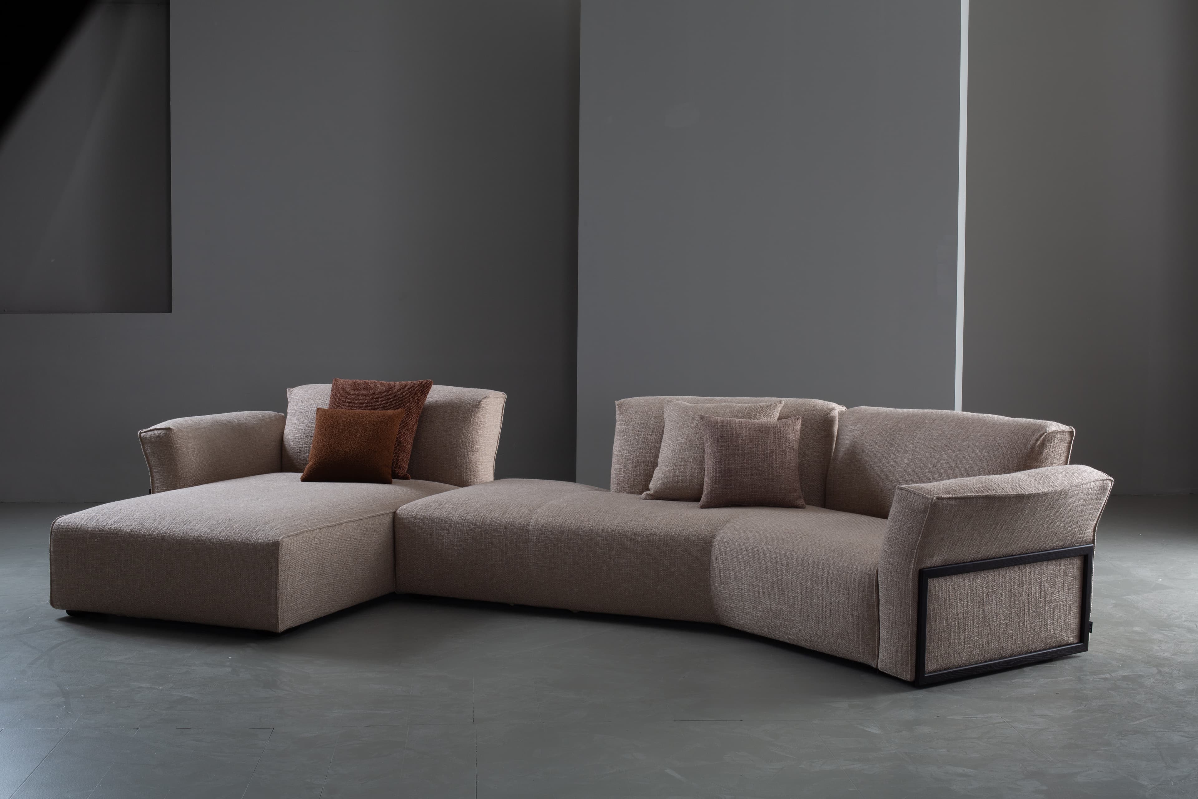 A contemporary modular sectional sofa upholstered in a light beige textured fabric, featuring a left-hand chaise lounge and a right-hand armrest with a distinctive dark framed detail. It is adorned with several brown and beige throw pillows. — 3D model