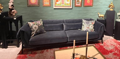 A contemporary gray fabric sofa featuring a minimalist design with a visible black metal frame. The sofa has two large seat cushions and two back cushions, complemented by gracefully rolled armrests that extend to meet the base frame. Two decorative throw pillows with a multi-colored floral pattern are placed on the sofa, adding a touch of visual interest. The overall aesthetic is clean and modern. — 3D model
