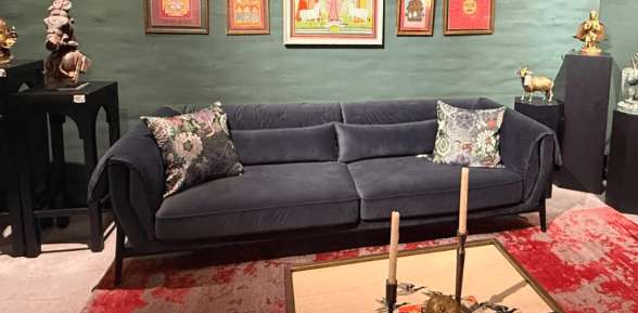A contemporary gray fabric sofa featuring a minimalist design with a visible black metal frame. The sofa has two large seat cushions and two back cushions, complemented by gracefully rolled armrests that extend to meet the base frame. Two decorative throw pillows with a multi-colored floral pattern are placed on the sofa, adding a touch of visual interest. The overall aesthetic is clean and modern. — 3D model