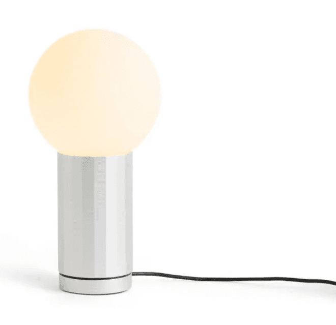 A modern table lamp featuring a spherical, frosted glass diffuser atop a cylindrical base with vertical fluting. The base is light-colored, possibly silver or white, and a black power cord extends from its bottom. The lamp is illuminated, emitting a soft, diffuse light. — 3D model