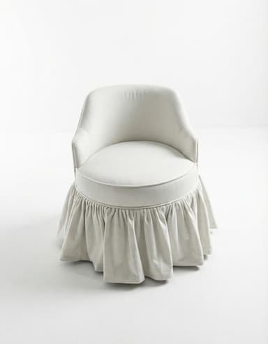 A compact, fully upholstered chair with a rounded back, low armrests, and a distinctive ruffled skirt covering its base, presented in a light, neutral fabric. — 3D model