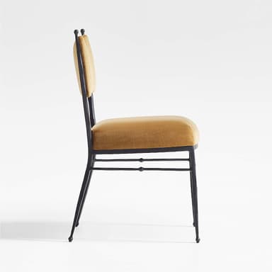 A chair with a dark, metallic frame and a cushioned seat and back. The frame appears to be wrought iron or a similar metal, with four slender legs and a simple stretcher system. The backrest is slightly curved and has a distinctive shape, reminiscent of a butterfly or a stylized 'W'. The upholstery is a rich, golden-brown velvet fabric. — 3D model