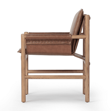 A contemporary armchair with a wooden frame and leather upholstery. The frame consists of four cylindrical legs connected by horizontal supports, forming a simple yet sturdy structure. The seat and backrest are upholstered in brown leather, with the armrests also featuring leather coverings with decorative stitching. The overall design suggests a blend of rustic and modern aesthetics. — 3D model