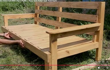 A natural light-toned wooden outdoor bench with a slatted seat, backrest, and armrests. The construction appears sturdy, featuring visible screw fastenings and simple rectangular legs. The design is utilitarian and well-suited for outdoor environments, suggesting resistance to elements or the need for outdoor-specific wood treatment. It lacks any upholstery or decorative elements, emphasizing its functional form. — 3D model