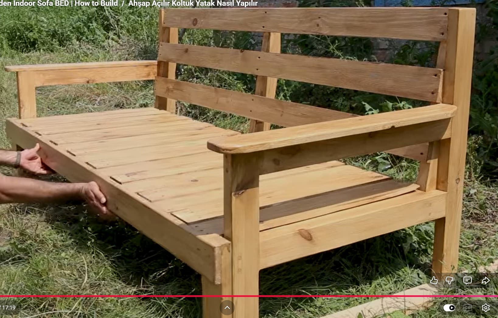 A natural light-toned wooden outdoor bench with a slatted seat, backrest, and armrests. The construction appears sturdy, featuring visible screw fastenings and simple rectangular legs. The design is utilitarian and well-suited for outdoor environments, suggesting resistance to elements or the need for outdoor-specific wood treatment. It lacks any upholstery or decorative elements, emphasizing its functional form. — 3D model