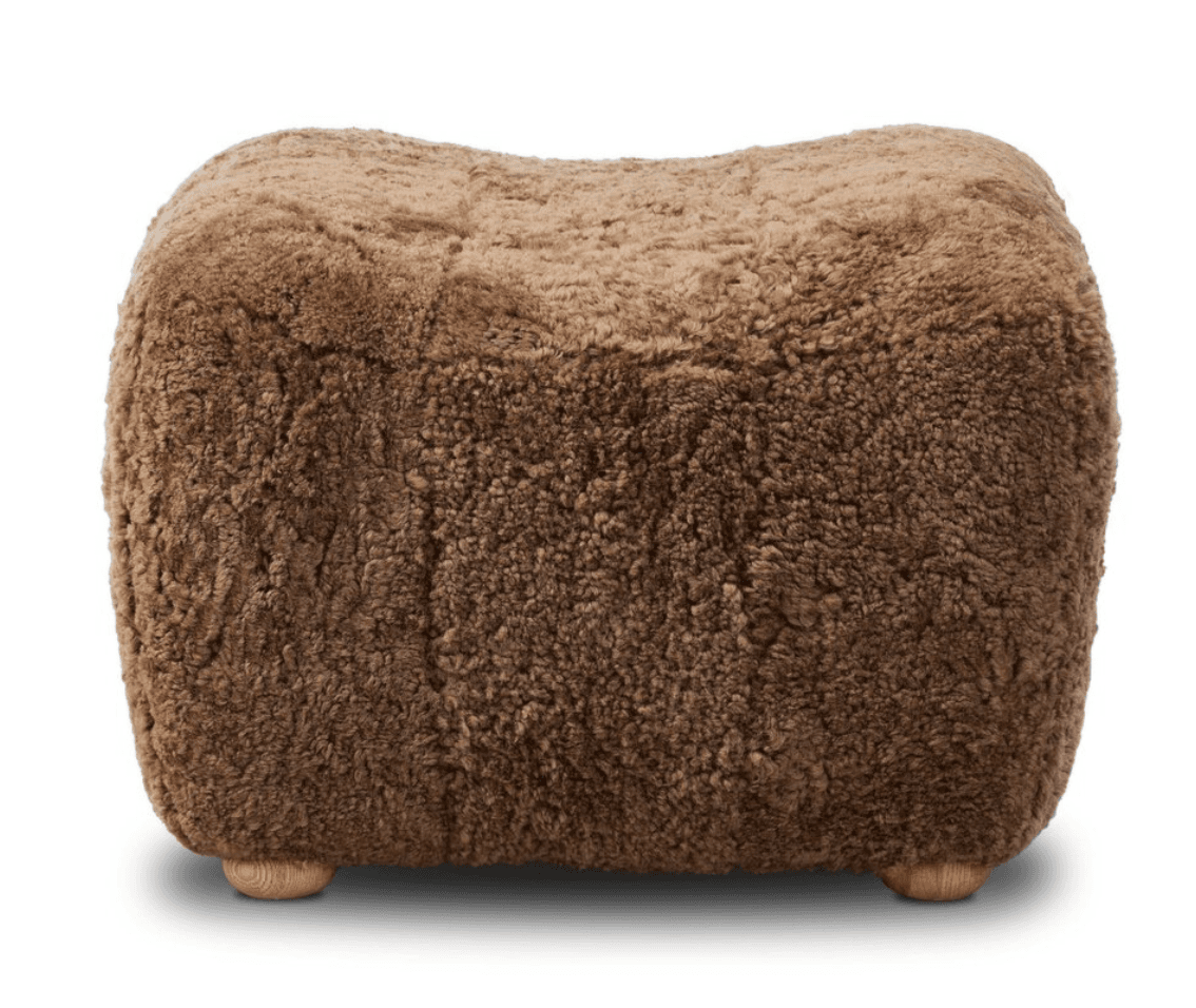 A rectangular, heavily upholstered ottoman or footstool, entirely covered in shaggy brown sheepskin or high-pile faux fur. The top surface features a subtle concave curve, while the base is supported by four small, round, light-toned wooden legs that are largely recessed beneath the body of the piece. — 3D model