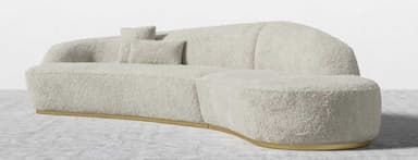A contemporary, sculptural sofa featuring a deeply curved and organic silhouette, fully upholstered in a textured, cream-colored boucle fabric. The design includes integrated backrest elements that flow seamlessly from the main body. It is supported by a recessed, polished brass plinth base, giving it a floating appearance. — 3D model