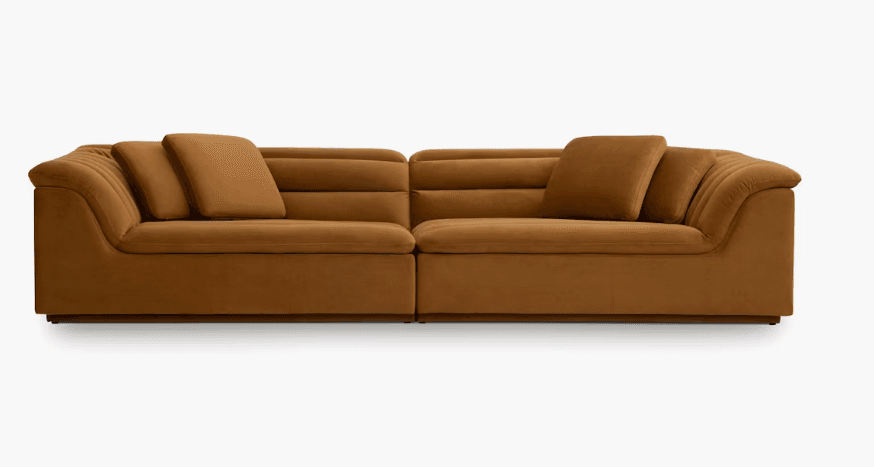 A two-piece modular sofa upholstered in a soft, textured fabric with a warm brown or caramel color. The design features horizontal channel tufting on the backrests and arms. It includes loose accent pillows for added comfort. The sofa has a low profile with a visible base. — 3D model