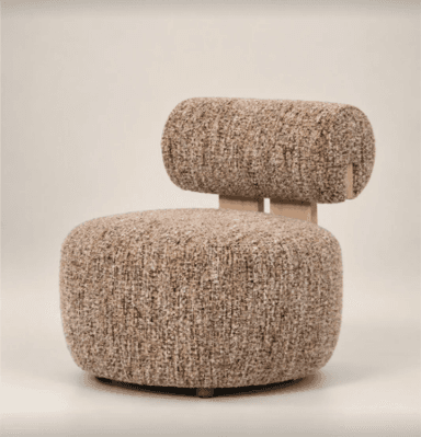 An armless lounge chair upholstered in a textured, light brown bouclé fabric. The design features a plush, rounded seat and a distinct cylindrical backrest supported by minimalist wooden elements, contributing to its modern and organic aesthetic. — 3D model