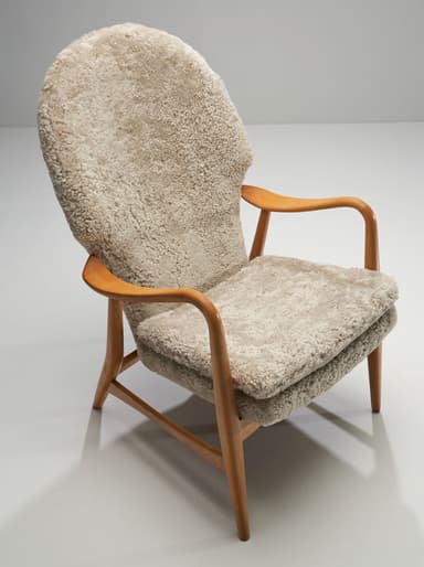 A high-backed armchair with a wooden frame and plush sheepskin upholstery. The frame consists of curved wooden arms and legs. The seat and back are fully upholstered in a textured, cream-colored sheepskin material, giving it a soft and inviting appearance. The design suggests a focus on comfort and organic forms. — 3D model