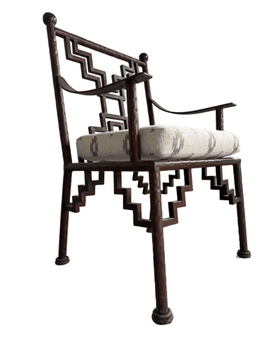 An armchair with a dark brown, possibly metal, frame featuring a geometric, stepped pattern on the back and legs. It has curved armrests and a cushioned seat upholstered in a textured fabric with a geometric pattern in shades of beige, brown, and grey. The chair has a decorative finial at the top of each back leg and round feet. — 3D model