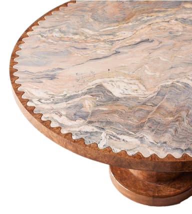 A close-up view of a table section, showcasing a round top with a decorative, scalloped edge. The tabletop features a complex pattern of swirling natural stone, incorporating shades of beige, pink, grey, and brown. The base, visible at the bottom, is made of wood and has a curved, layered design. — 3D model