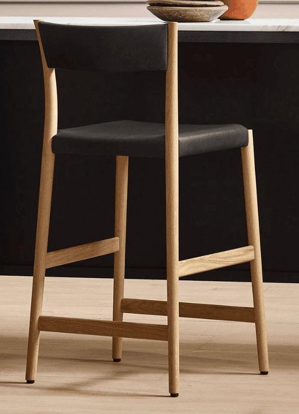 A contemporary bar stool with a wooden frame and a black upholstered seat and backrest. The stool features a curved backrest that extends from the frame. The legs are made of light-colored wood and are connected by horizontal support rails, providing stability. The seat and backrest appear to be upholstered in a dark, possibly leather, material. — 3D model
