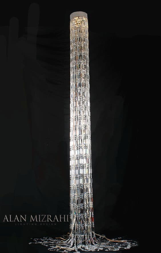 A tall, slender, modern floor lamp featuring a cylindrical design composed of numerous clear, faceted elements that create a sparkling, crystal-like effect. The internal light source illuminates these elements, diffusing light elegantly. The top and bottom appear to have a solid, opaque finish, likely white or silver-toned, providing a clean contrast to the clear body. — 3D model