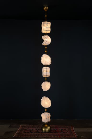 A tall, vertically oriented chandelier featuring multiple tiers of irregularly shaped diffusers made of a translucent material, interspersed with metallic elements, all suspended from a central rod. — 3D model