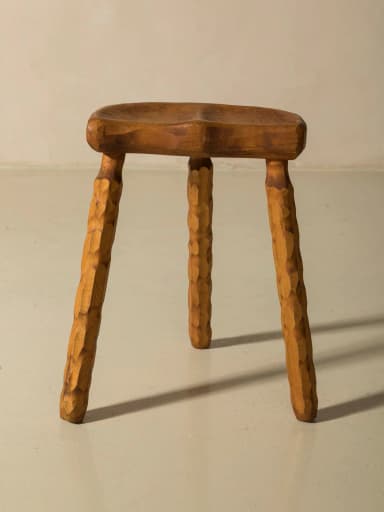 A three-legged wooden stool with an oval, contoured seat. The legs are carved with a textured pattern, giving them a rustic appearance. The overall design is simple and organic. — 3D model