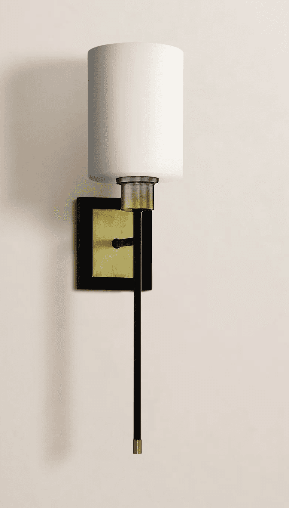 A modern wall lamp with a cylindrical white shade. The lamp features a black metal arm extending downwards from a square backplate that has a brass accent. The shade is attached to the arm via a brass fixture. The overall design is minimalist and contemporary. — 3D model