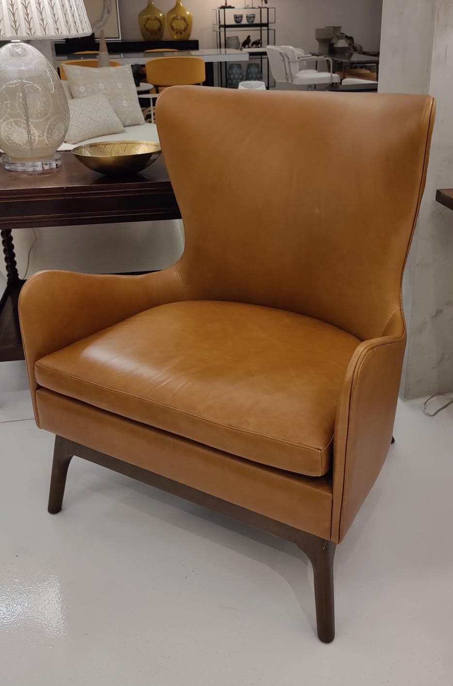 A contemporary high-back armchair upholstered in tan leather, featuring a comfortable padded seat cushion, integrated armrests, and four slender tapered dark wood legs. — 3D model