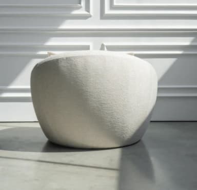 A contemporary lounge chair with a rounded, organic silhouette, fully upholstered in a textured, off-white fabric, and featuring a loose back cushion. — 3D model
