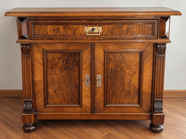 A traditional, dark wooden accent cabinet featuring a single drawer above two hinged doors, adorned with decorative brass hardware and carved pilasters. The cabinet rests on four bun feet. — 3D model