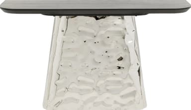 A modern console table featuring a dark, elongated rectangular top with gently rounded edges, supported by a substantial, polished hammered metal base. The base has a distinctive, irregular, and textured surface, giving it a unique sculptural quality. Its form tapers slightly, widening towards the bottom for enhanced stability and visual presence. — 3D model