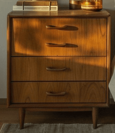 A light-toned wooden nightstand featuring three drawers, rounded edges, integrated carved pulls, and four splayed, tapered legs, indicative of a Mid-Century Modern design aesthetic. — 3D model