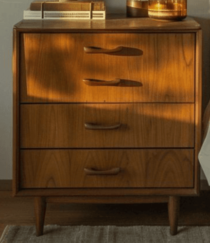 A light-toned wooden nightstand featuring three drawers, rounded edges, integrated carved pulls, and four splayed, tapered legs, indicative of a Mid-Century Modern design aesthetic. — 3D model