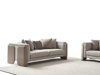 A contemporary three-seater sofa upholstered in a light greige fabric with distinctive wide, padded armrests featuring textured taupe side panels. The sofa has loose seat cushions and comes with an assortment of toss pillows in complementary greige and taupe tones, some with textured patterns. — 3D model