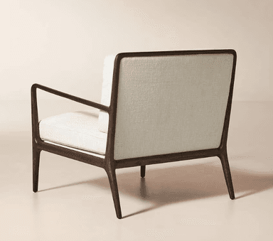 A contemporary armchair featuring a dark wood frame with a warm finish. The frame has a streamlined design with gently curved armrests that extend from the back. The chair is upholstered in a textured, off-white fabric on the seat, back cushion, and armrest pads. The overall design is minimalist and elegant, suitable for modern interiors. — 3D model