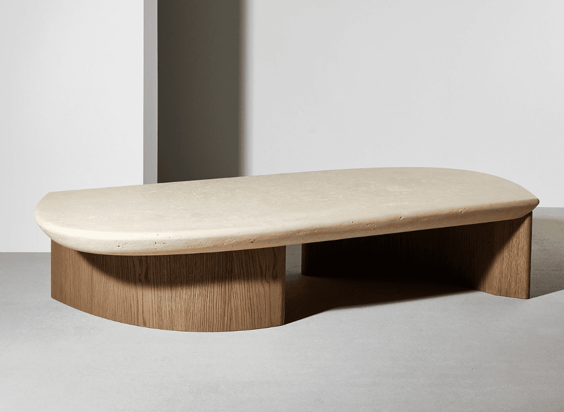 A contemporary coffee table featuring a thick, rounded, irregular-shaped top and a contrasting base. The tabletop appears to be made of a light-colored, textured material, possibly stone or a composite, with a matte finish. The base consists of two curved wooden elements, likely veneered or solid wood with a visible grain pattern, providing a substantial support structure. The overall design is minimalist and sculptural. — 3D model