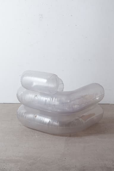 An inflatable armchair with a distinct translucent, smoky brown hue. The design features large, cylindrical forms for the armrests, base, and backrest, creating a plush and rounded silhouette. Seams are visible where the inflatable sections are joined, indicating its construction method. The material appears to be a flexible plastic or vinyl. — 3D model