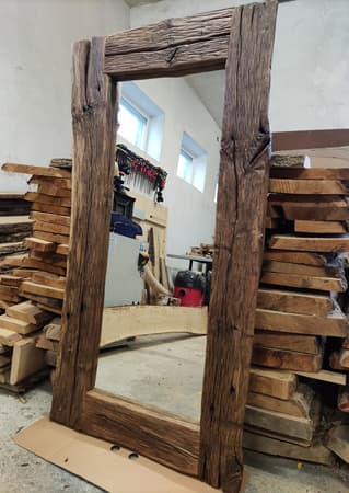 A rectangular mirror with a frame made of rough, weathered wood. The wood appears to be reclaimed, showing natural imperfections, knots, and a rustic texture. The frame has an uneven, organic edge, contributing to its primitive style. The mirror surface is flat and reflective. — 3D model