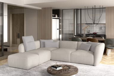 A large, L-shaped sectional sofa with a low profile and rounded edges. It is upholstered in a textured, light-colored fabric and features several throw pillows. The sofa is placed on a light gray rug in a living area. — 3D model