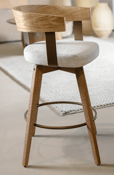 A modern swivel bar stool featuring a light-toned wooden frame, a plush upholstered seat, and a distinctive curved wooden backrest. It stands on four tapered wooden legs, reinforced by a circular metal footrest, and features a visible swivel mechanism. — 3D model