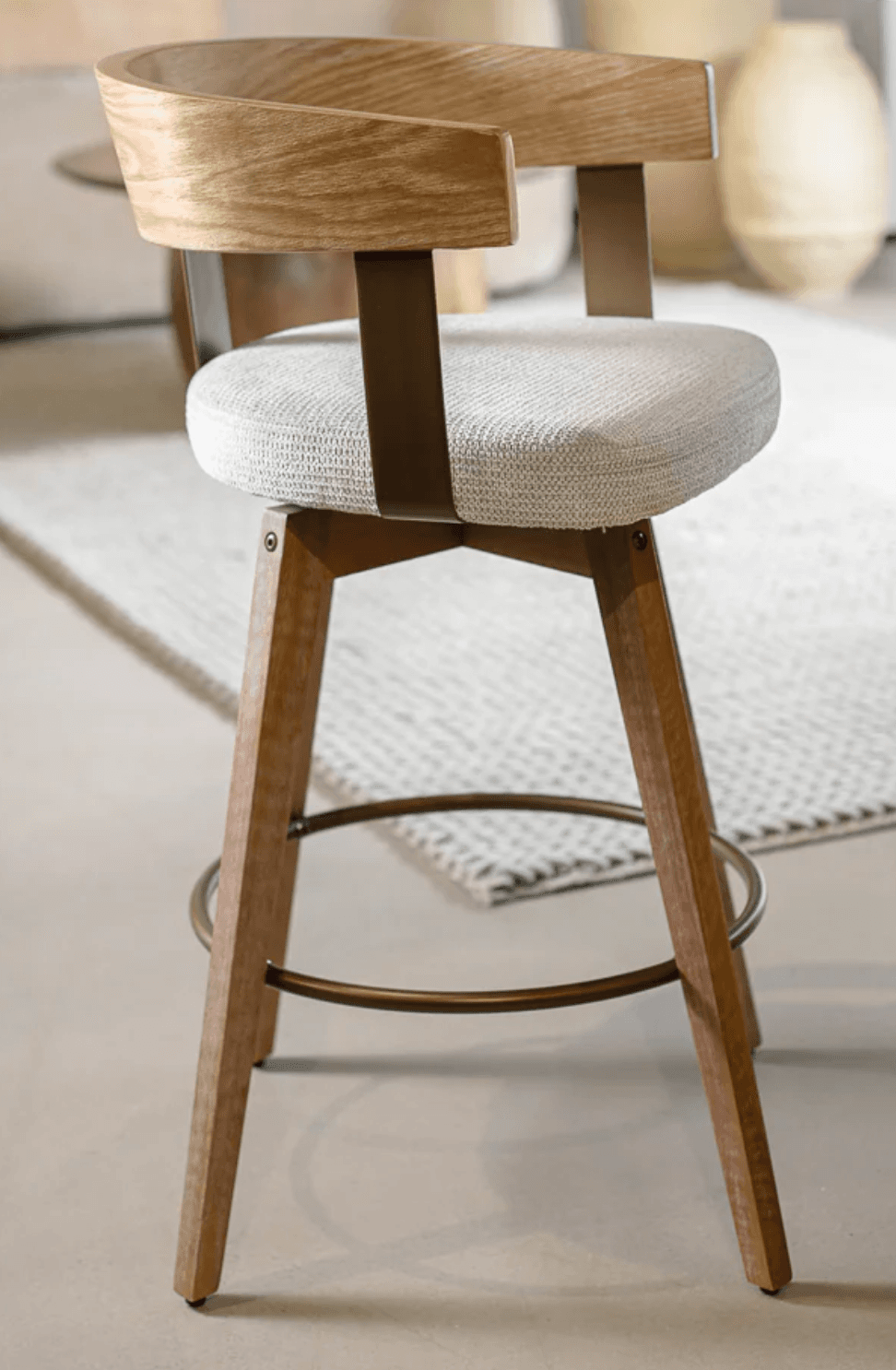 A modern swivel bar stool featuring a light-toned wooden frame, a plush upholstered seat, and a distinctive curved wooden backrest. It stands on four tapered wooden legs, reinforced by a circular metal footrest, and features a visible swivel mechanism. — 3D model